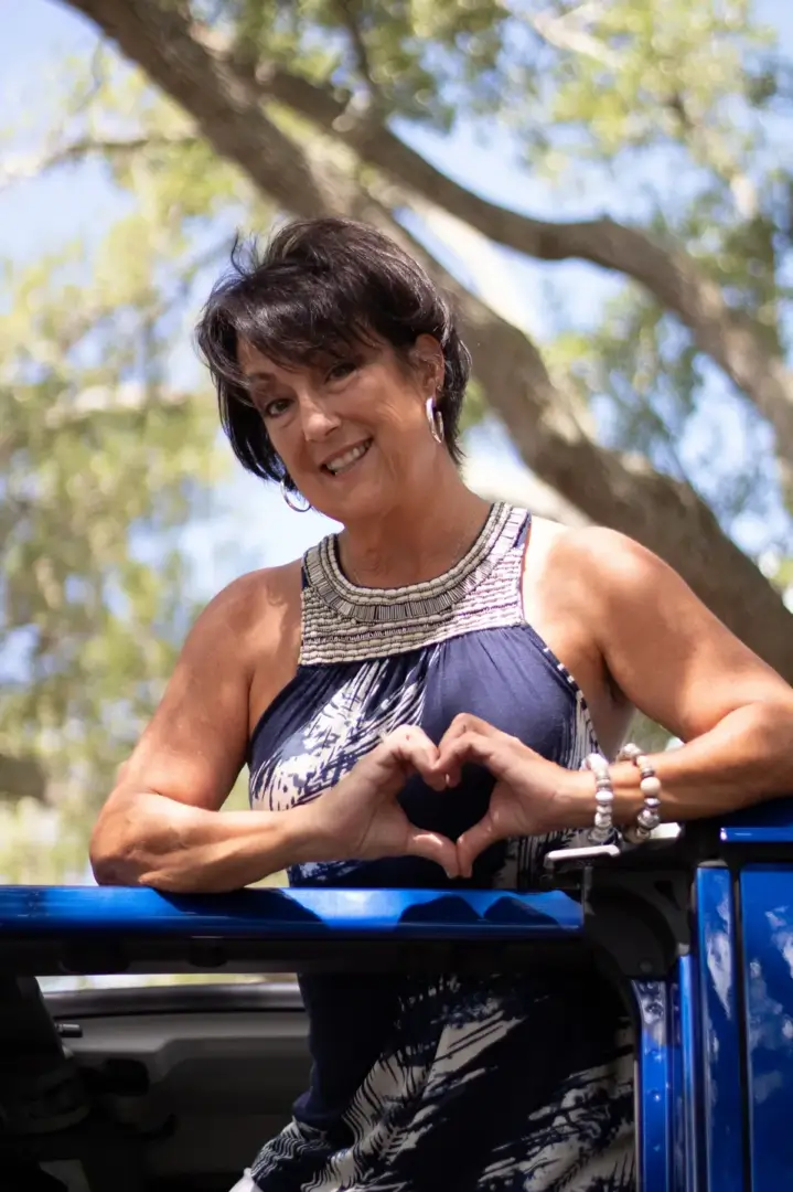 A woman making an i love you sign on top of a park bench.